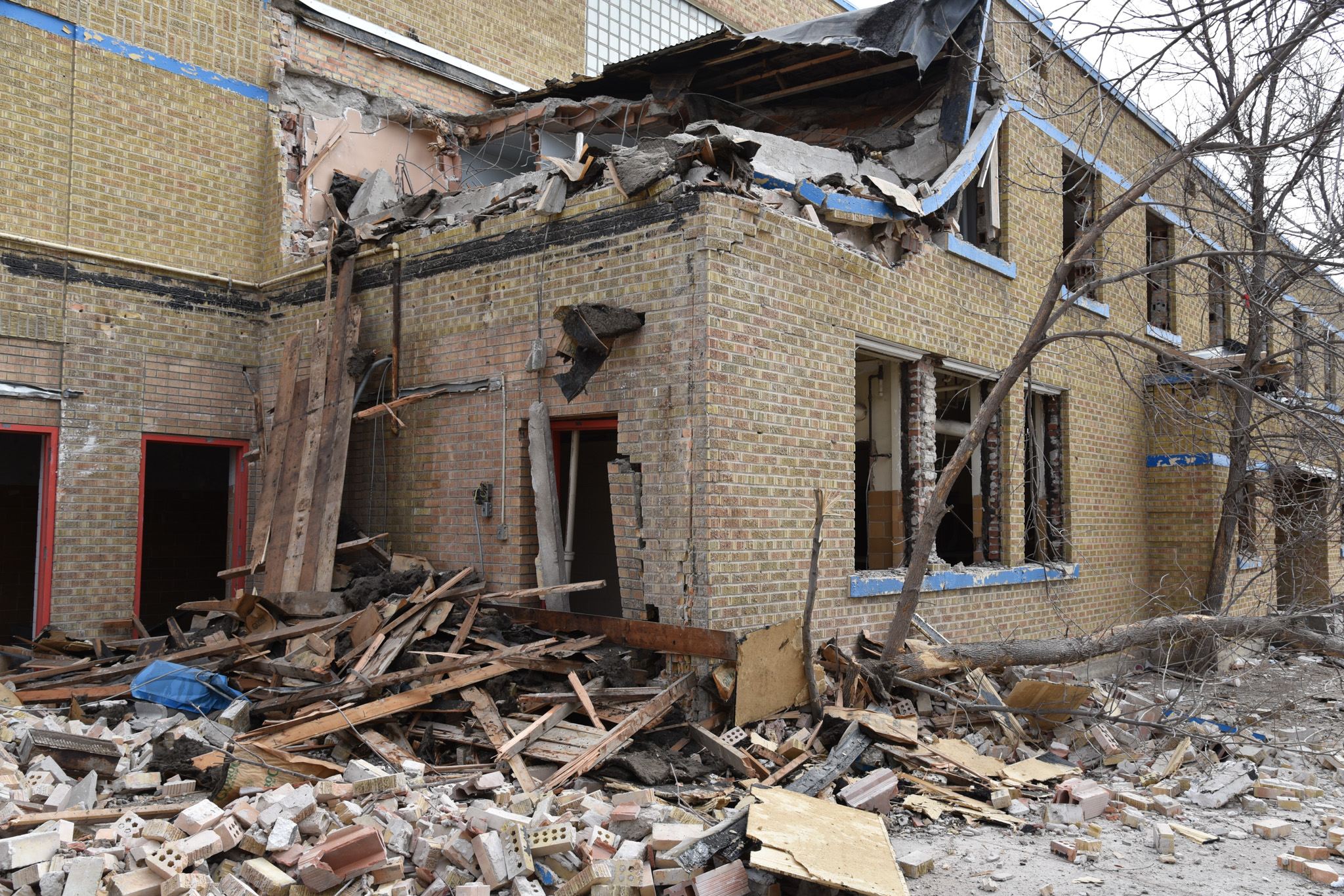 Damaged brick building with debris and fallen tree.