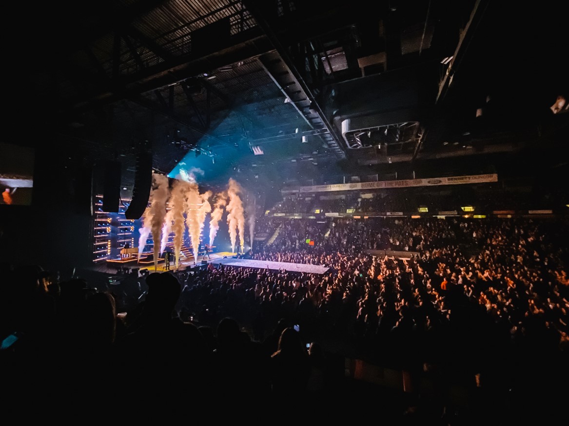 Crowd cheering at indoor concert with stage lights.