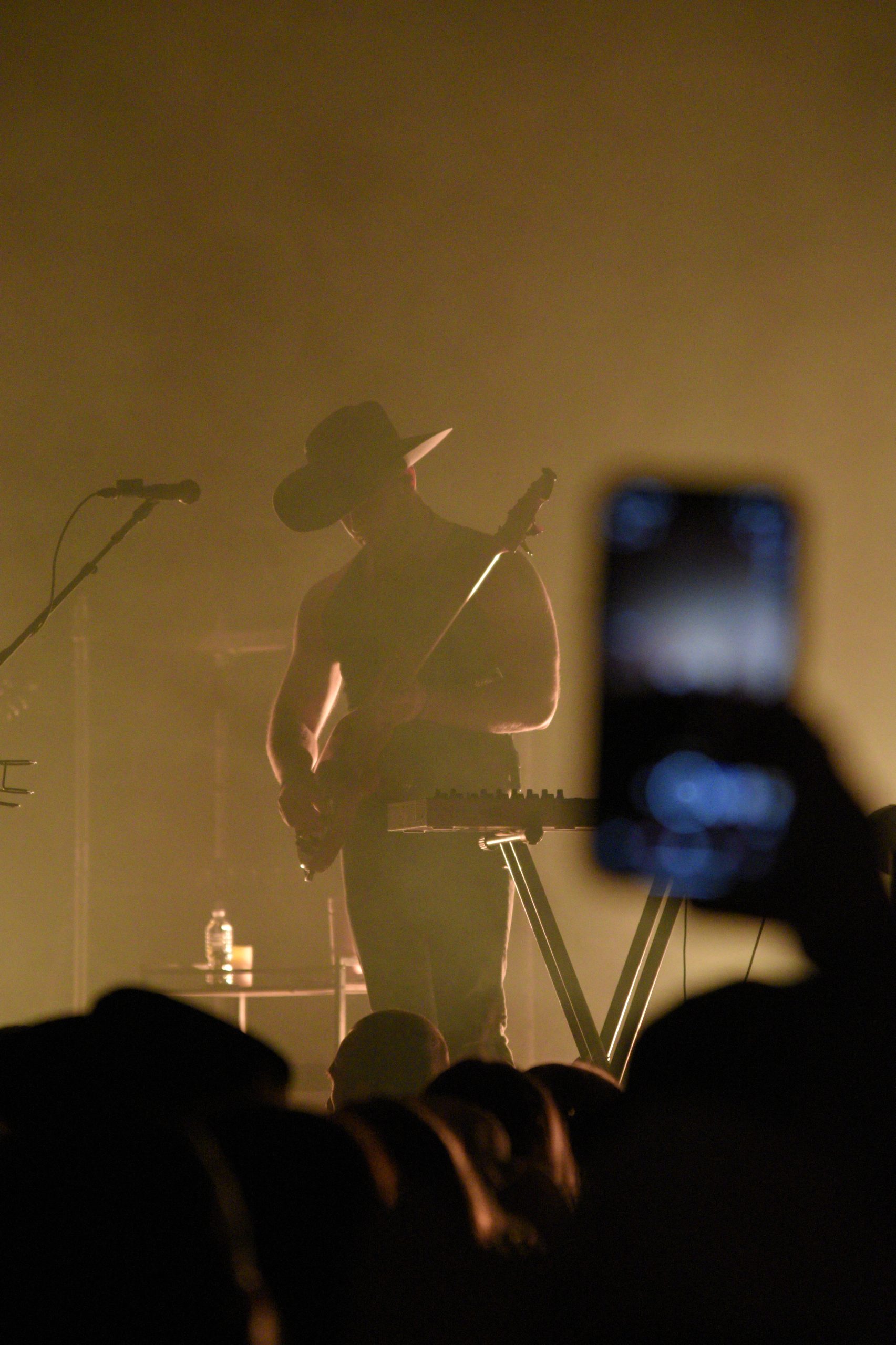 Silhouetted guitarist performs on stage with phone recording.