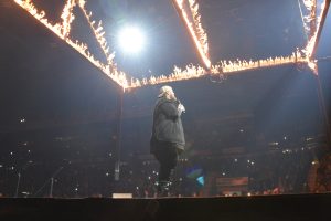 Performer on stage with flaming lights at concert.