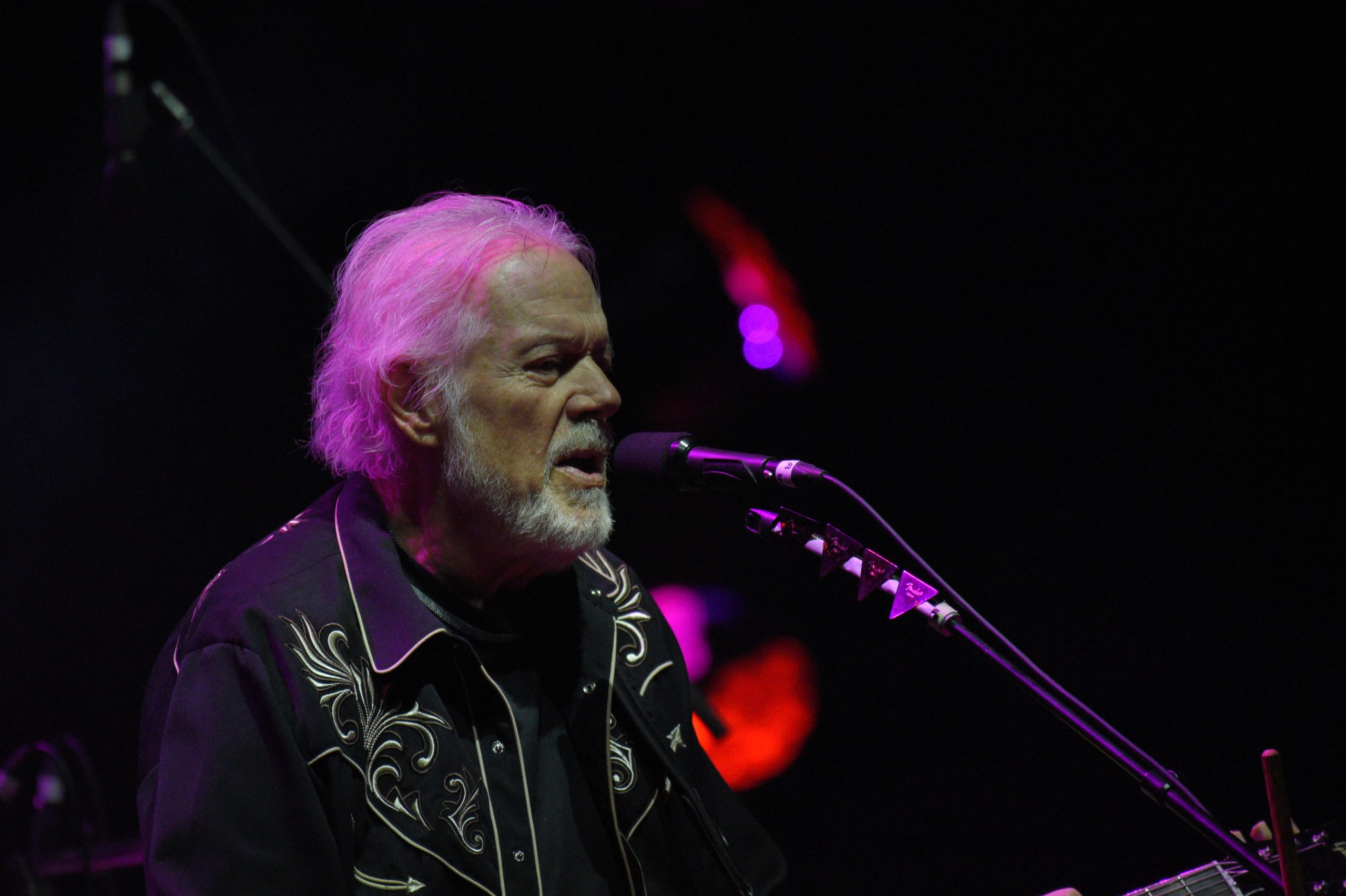 Man performing on stage with microphone and guitar.