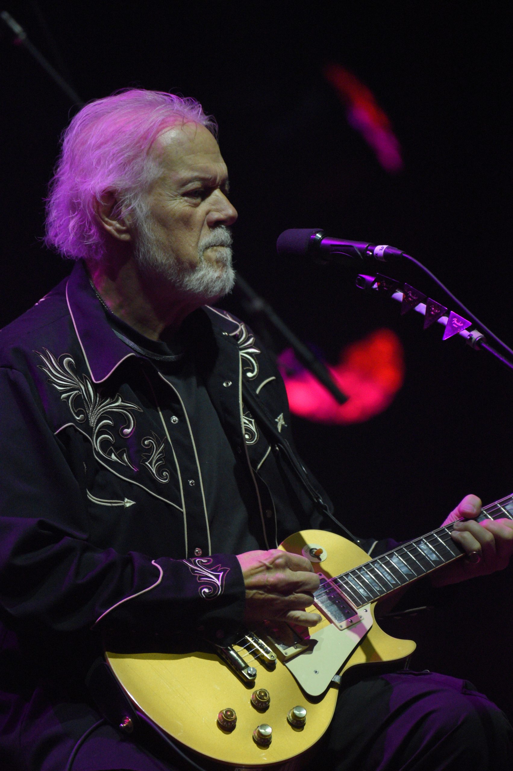 Older man playing yellow electric guitar on stage.