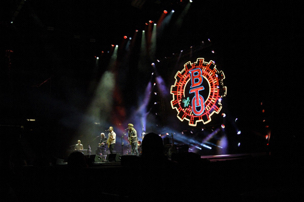 Band performing with large illuminated BT logo on stage.