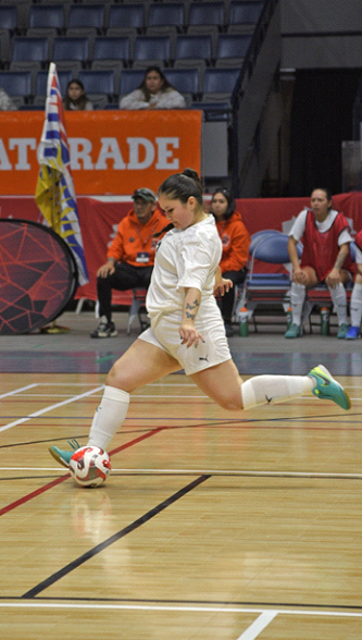 Woman in white jersey kicks futsal ball indoors.