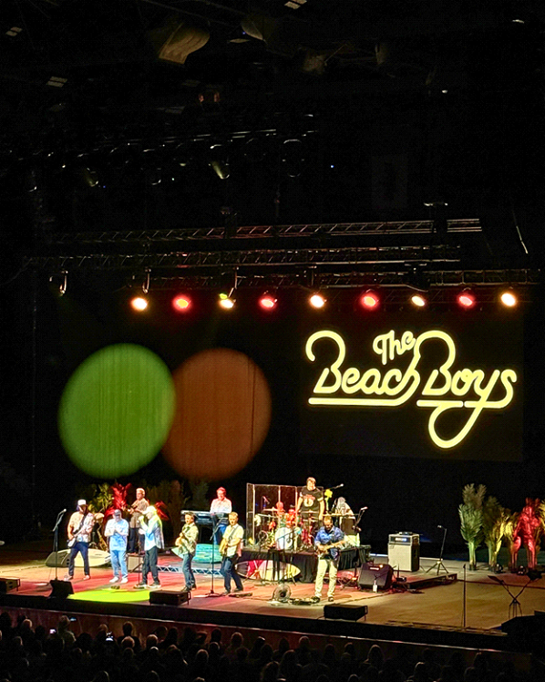 Band performing on stage with The Beach Boys sign.