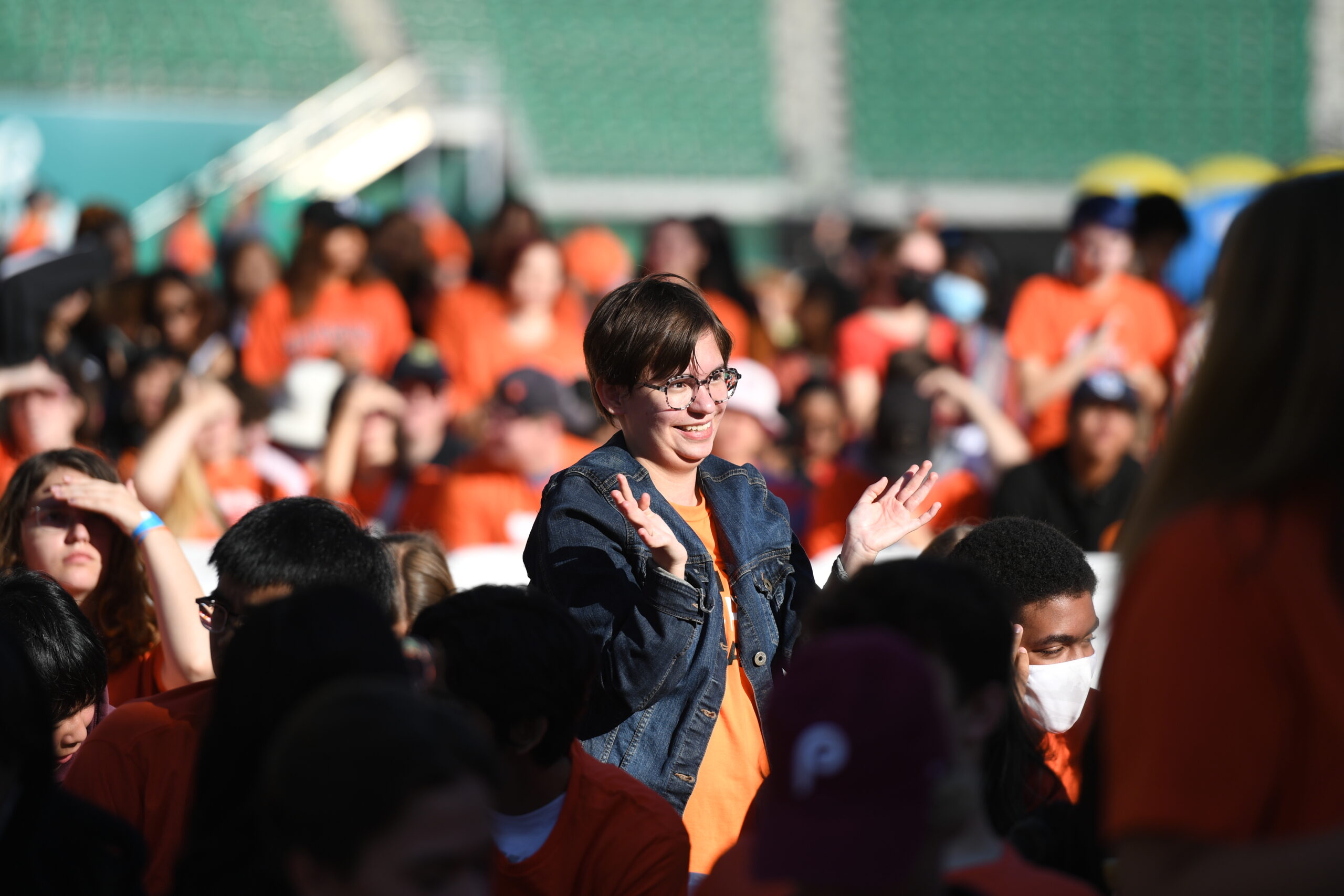 Person in denim jacket amidst crowd, smiling.