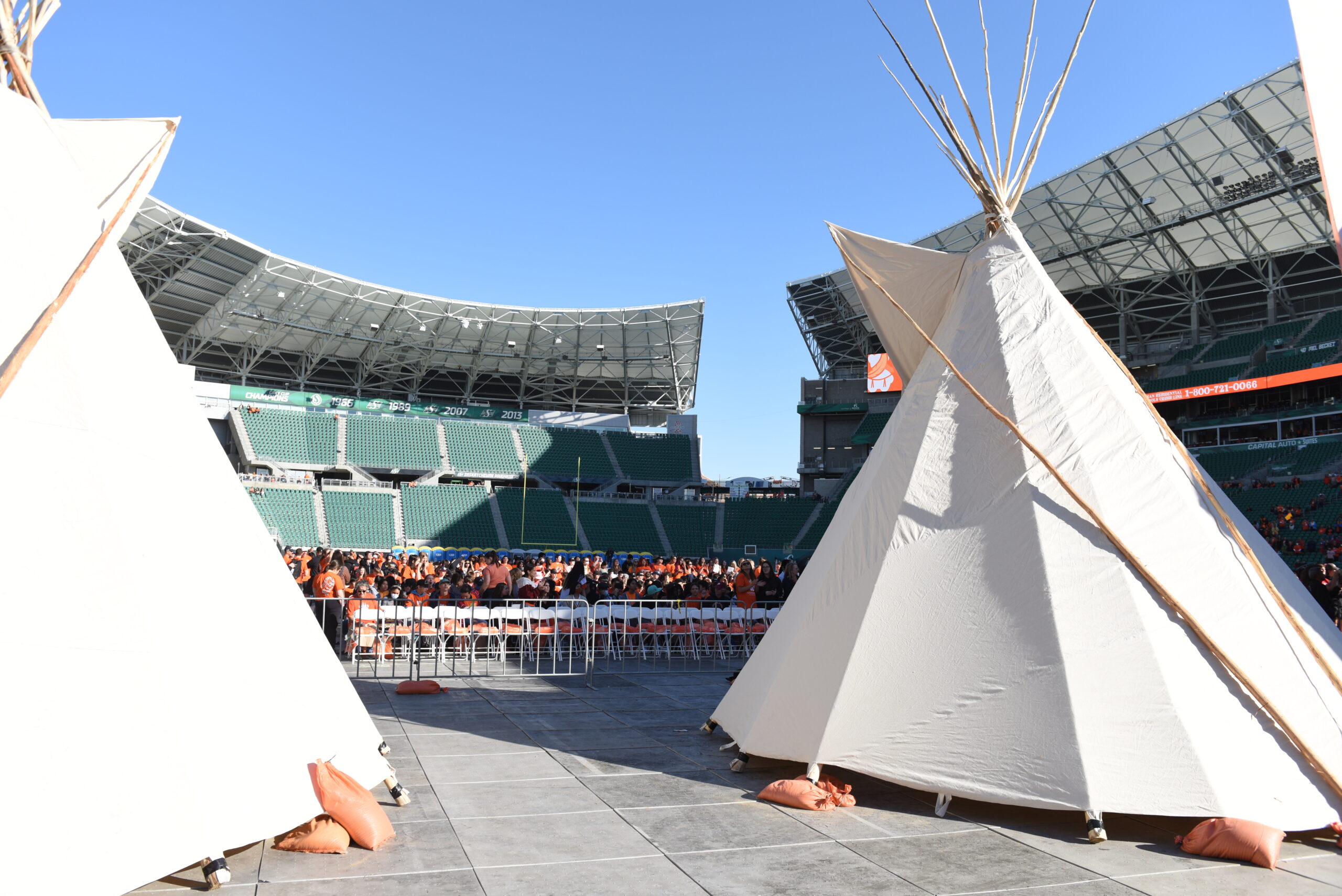 Teepees at outdoor stadium event with crowd.