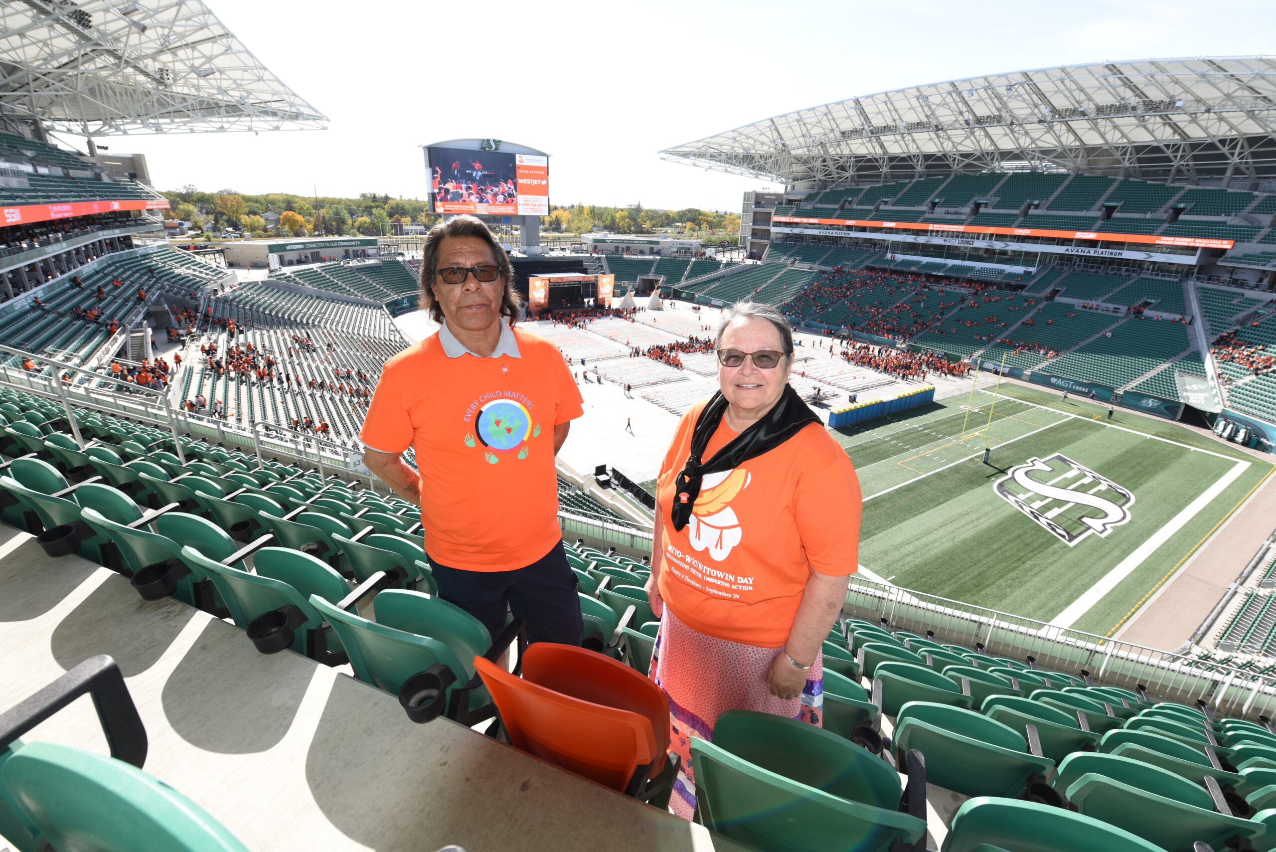 Two people in orange shirts at stadium event.