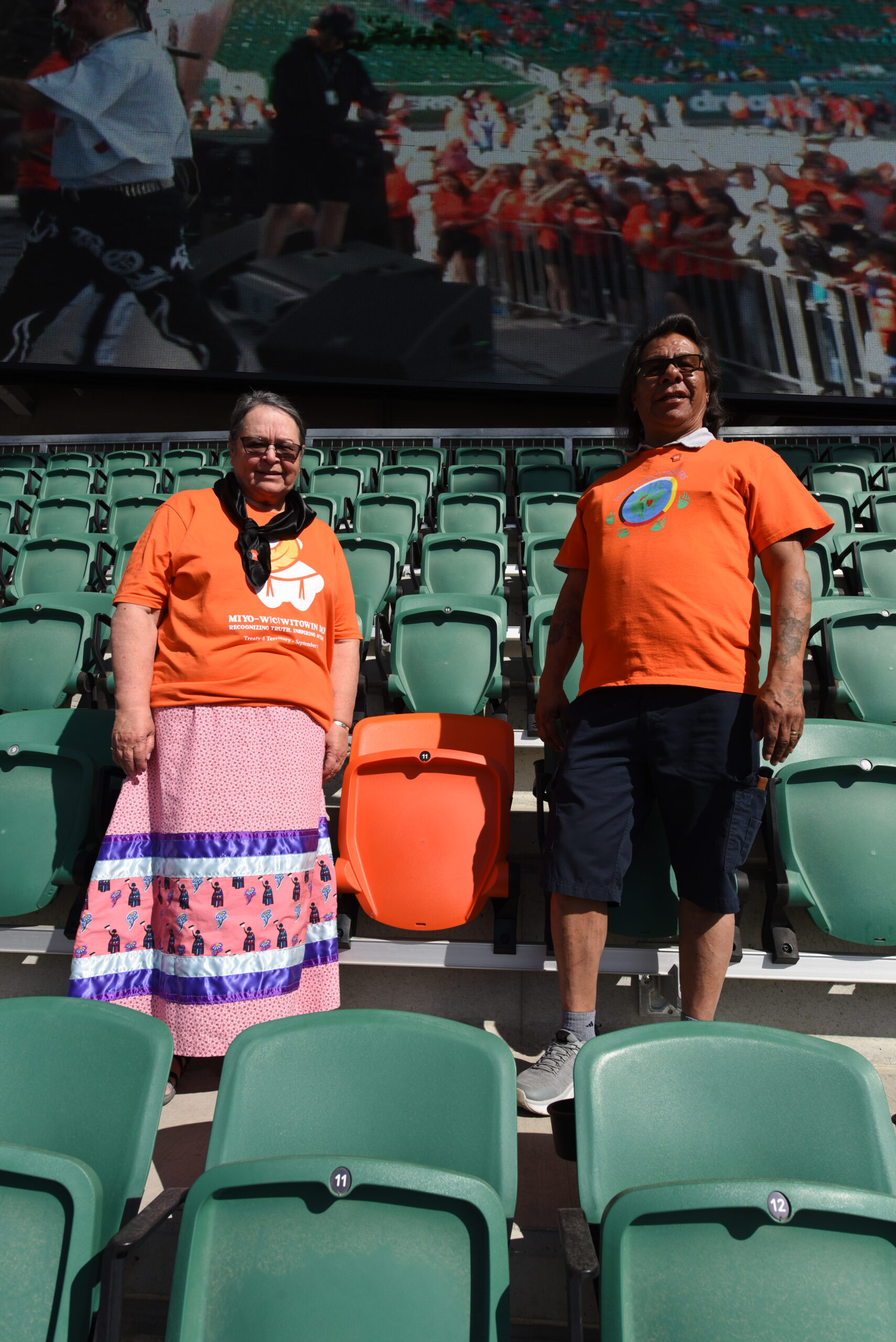 Two people wearing orange shirts in stadium seats.