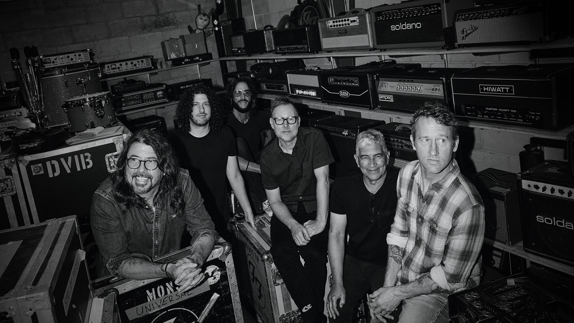 Band members in recording studio surrounded by amplifiers.